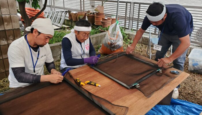 網戸を張替える穐元青年部長(左)と松井支部執行委員長(中央)=6月15日、日吉本町